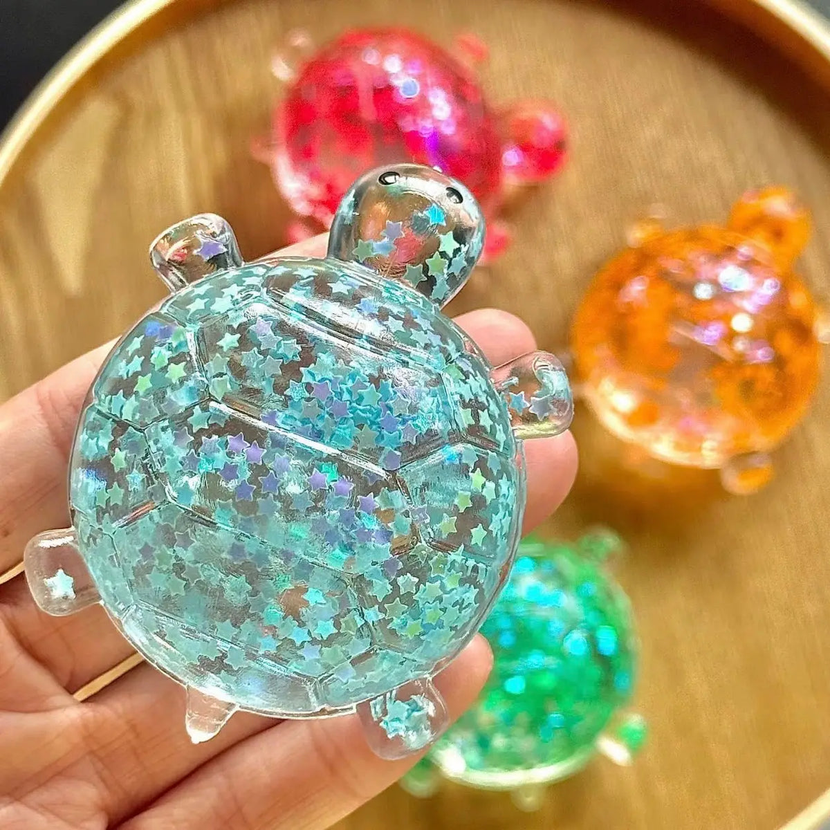 Glitter turtle squishy toy with holographic star glitter in teal, with additional colors in background