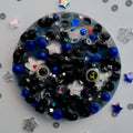 Treasure Cove Pick-Me Pad – overhead view of dark galaxy-themed sensory pad with black and blue beads, silver stars, and character charms